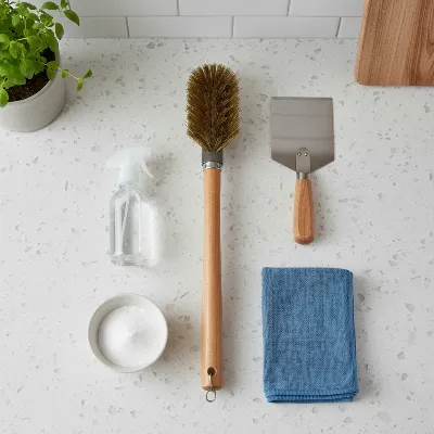 Essential cleaning tools for stone pizza oven maintenance laid out on a kitchen counter.