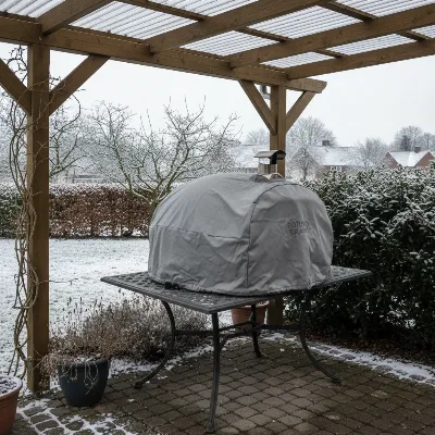Portable pizza oven stored securely under a covered patio with a fitted cover during winter